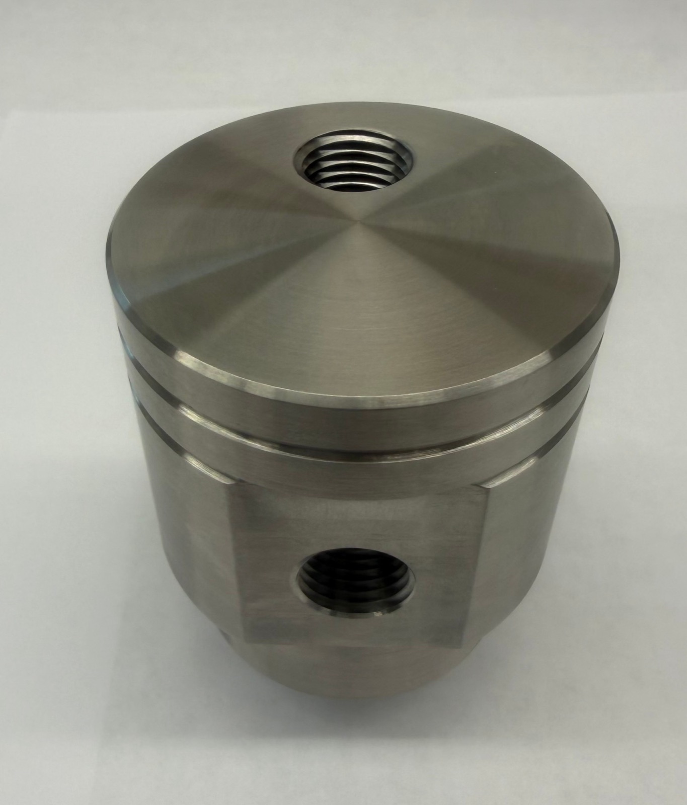 A machined cylindrical housing with a milled flat and two threaded ports